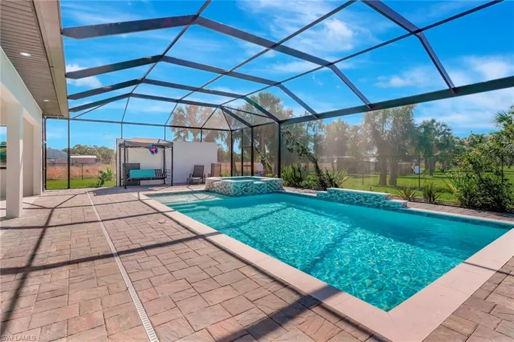 View of pool featuring a patio area, glass enclosure, a pool with connected hot tub, and fence