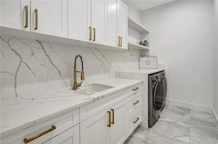 Laundry room featuring marble finish floor, baseboards, cabinet space, independent washer and dryer, and a sink