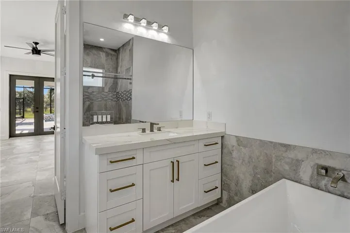 Full bathroom with vanity, tiled shower, a freestanding tub, ceiling fan, and french doors