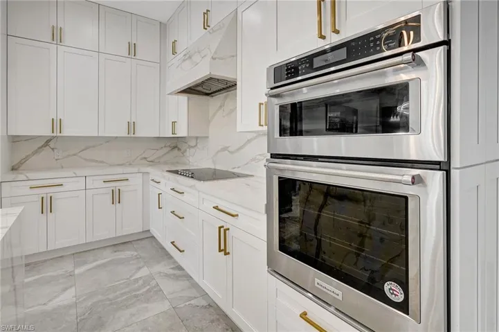 Kitchen featuring marble finish floor, under cabinet range hood, stainless steel double oven, black electric stovetop, and light stone countertops