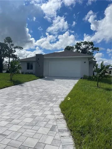 Single story home with a front yard, stucco siding, decorative driveway, and an attached garage