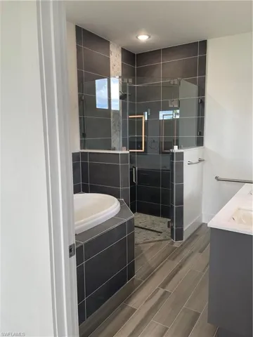 Bathroom with double vanity, a bath, a shower stall, and wood finish floors