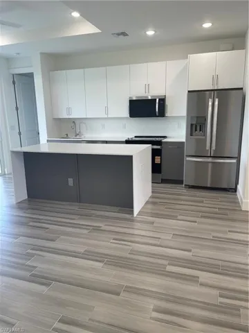 Kitchen featuring fridge, stove, white cabinets, recessed lighting, and wood tiled floors
