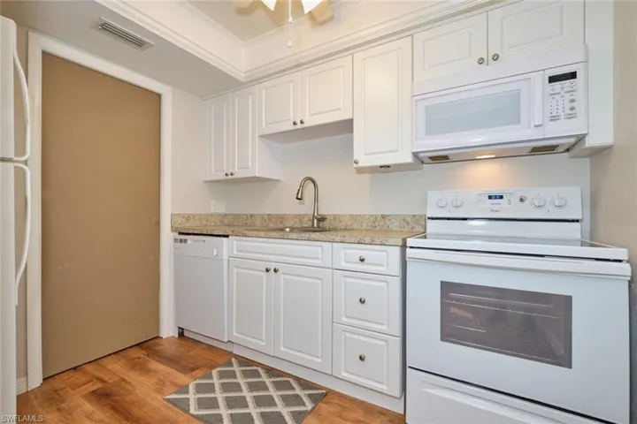 Kitchen with white appliances, tray ceiling, and white cabinetry.