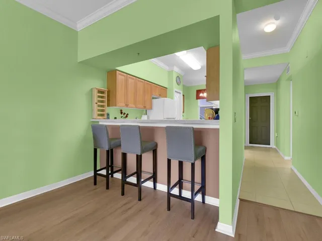 Kitchen with a kitchen bar, crown molding, baseboards, freestanding refrigerator, and light wood finished floors