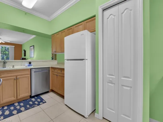 Kitchen featuring crown molding, dishwasher, light tile patterned floors, light countertops, and freestanding refrigerator