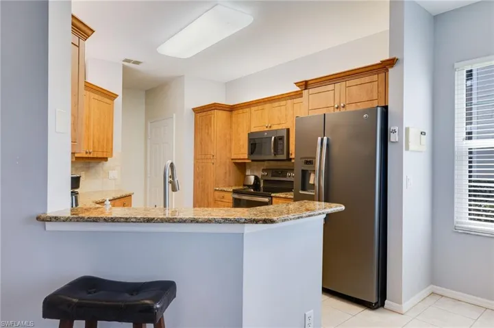 Kitchen with decorative backsplash, stainless steel appliances, a peninsula, light stone countertops, and a breakfast bar area