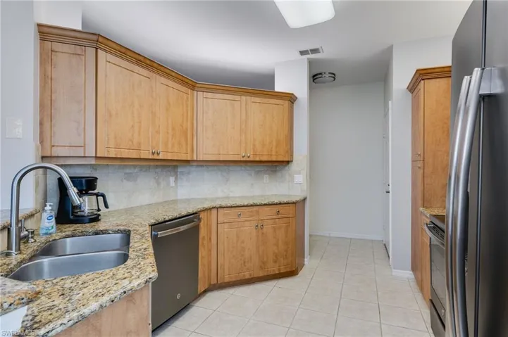 Kitchen with stainless steel appliances, tasteful backsplash, light stone counters, and light tile patterned flooring