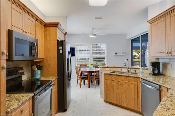 Kitchen featuring stainless steel appliances, backsplash, a peninsula, light stone countertops, and a ceiling fan