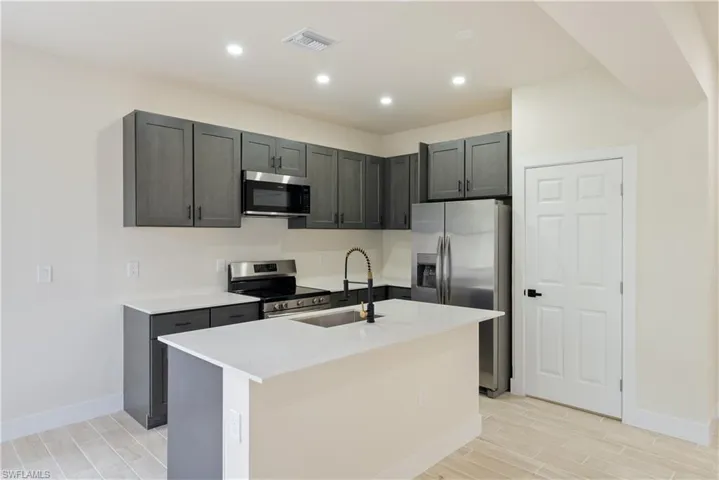 Kitchen featuring stainless steel appliances, wood tiled floors, a kitchen island with sink, light stone countertops, and recessed lighting