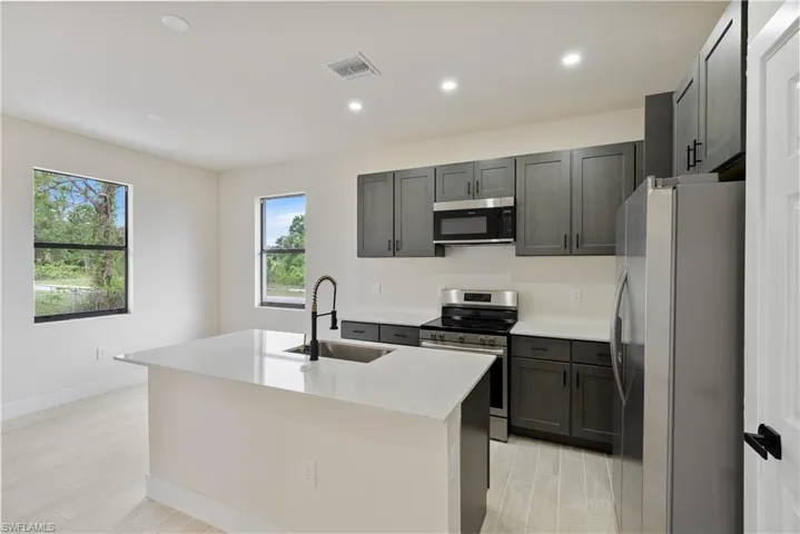 Kitchen with stainless steel appliances, recessed lighting, light stone counters, an island with sink, and light wood-type flooring
