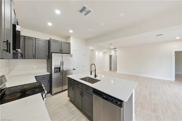 Kitchen with recessed lighting, stainless steel appliances, a kitchen island with sink, light stone countertops, and open floor plan