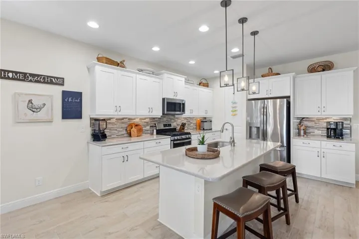 Kitchen featuring appliances with stainless steel finishes, light hardwood / wood-style floors, white cabinetry, sink, and a kitchen island with sink