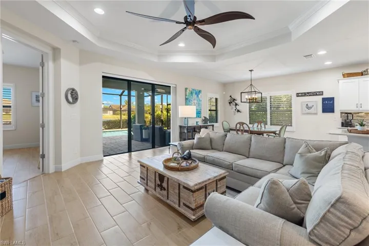 Living room featuring ceiling fan with notable chandelier, a raised ceiling, ornamental molding, and a healthy amount of sunlight