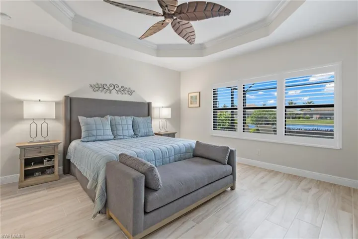 Bedroom featuring light wood-type flooring, a tray ceiling, ceiling fan, and crown molding