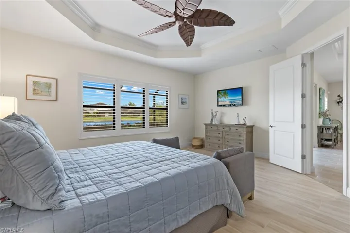 Bedroom with light wood-type flooring, a raised ceiling, crown molding, and ceiling fan