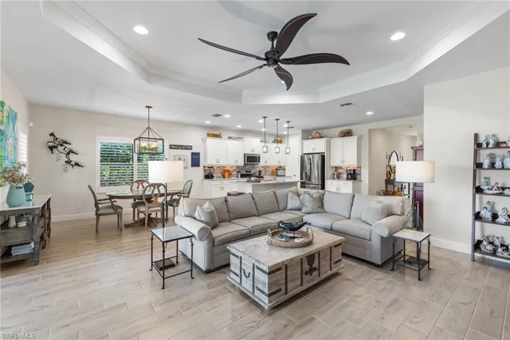 Living room featuring crown molding, light hardwood / wood-style flooring, ceiling fan with notable chandelier, and a tray ceiling