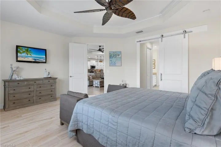 Bedroom featuring a barn door, ceiling fan, a raised ceiling, and light wood-type flooring