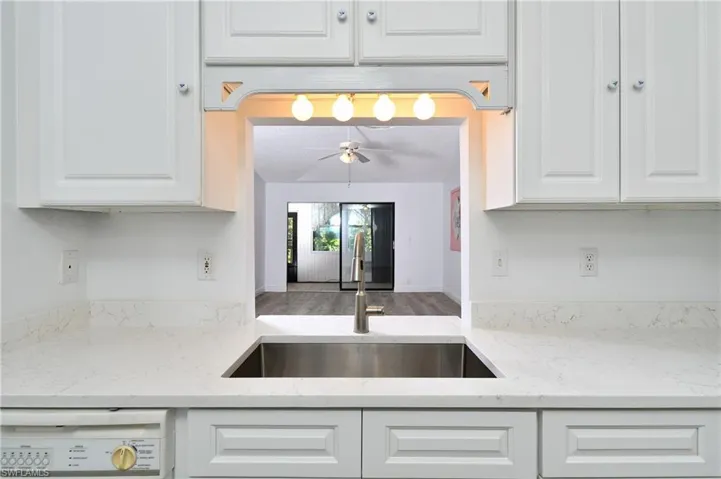 Kitchen featuring white cabinets, light stone counters, white dishwasher, and wood finished floors