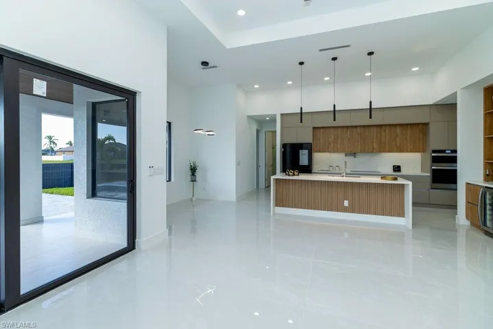 Kitchen featuring sink, fridge, pendant lighting, stainless steel double oven, and a large island