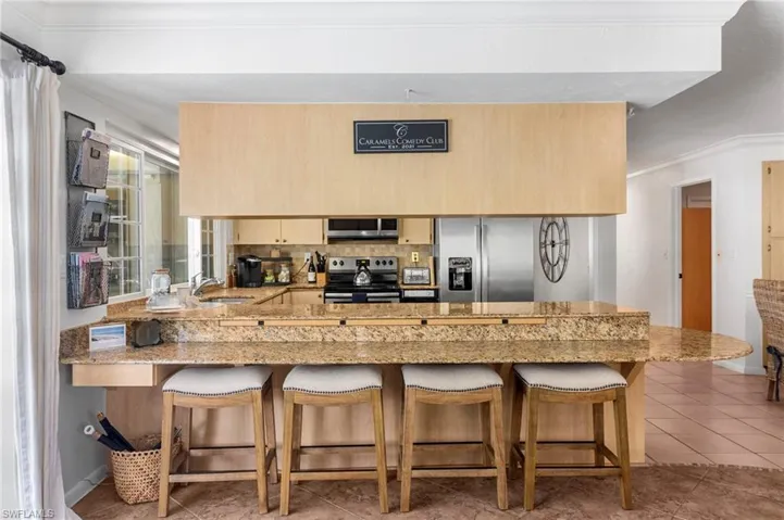 Kitchen with light brown cabinets, light tile patterned floors, kitchen peninsula, stainless steel appliances, and decorative backsplash