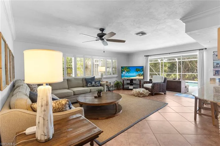 Living room with light tile patterned floors, a wealth of natural light, ceiling fan, and crown molding
