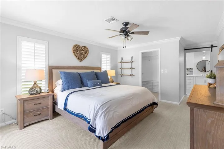 Bedroom with a closet, a barn door, light colored carpet, crown molding, and ceiling fan