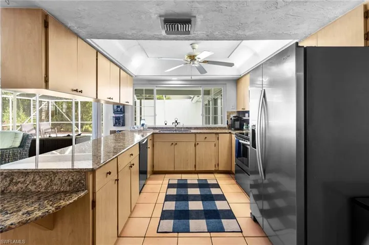 Kitchen featuring appliances with stainless steel finishes, stone counters, light tile patterned flooring, ceiling fan, and a raised ceiling