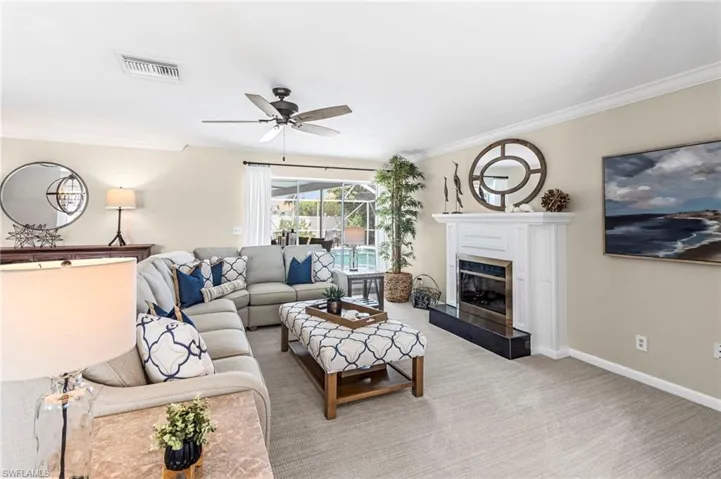Carpeted living room featuring crown molding, a fireplace, and ceiling fan