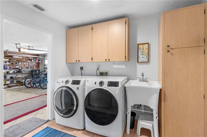Washroom with light tile patterned floors, independent washer and dryer, and cabinets