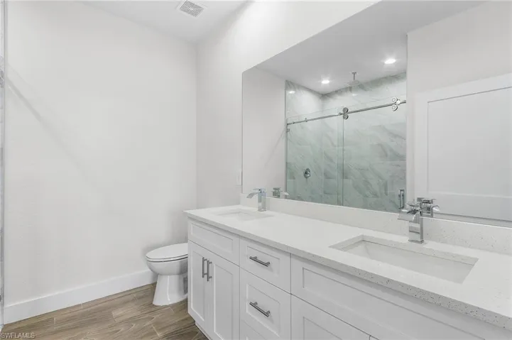 Bathroom featuring a tile shower, toilet, and dual bowl vanity