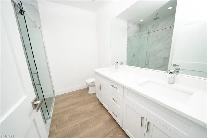 Bathroom featuring wood-type flooring, a shower with door, toilet, and dual bowl vanity
