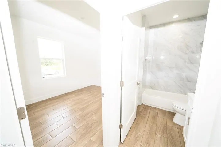 Bathroom with tiled shower / bath, wood-type flooring, and toilet