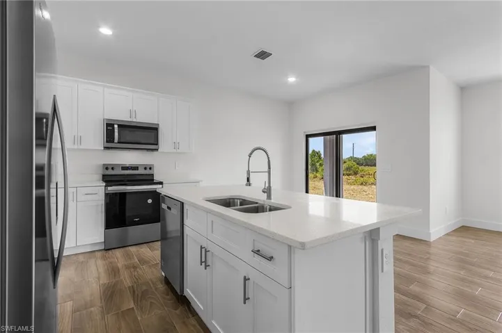 Kitchen featuring stainless steel appliances, white cabinets, hardwood / wood-style floors, sink, and a center island with sink
