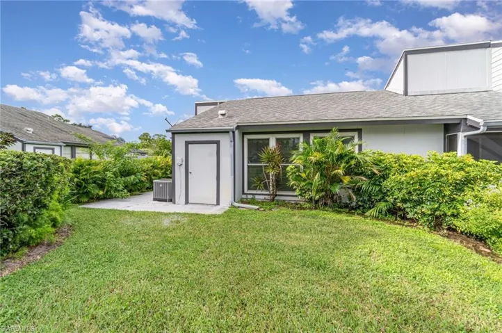 Rear view of property featuring roof with shingles, a lawn, and a patio area