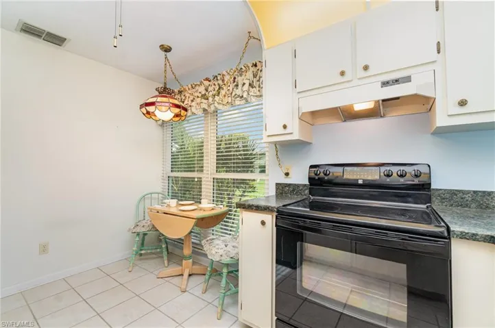 Kitchen with electric range, under cabinet range hood, light tile patterned flooring, white cabinetry, and decorative light fixtures