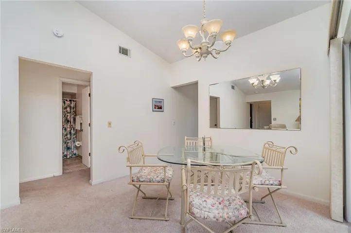 Dining area with light colored carpet, lofted ceiling, and a chandelier