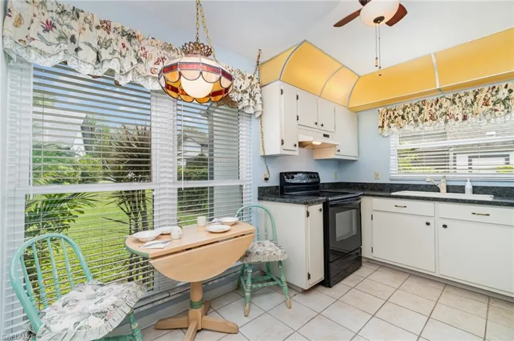 Kitchen with electric range, white cabinets, light tile patterned flooring, under cabinet range hood, and a ceiling fan