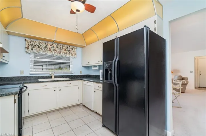 Kitchen featuring black appliances, dark countertops, white cabinetry, light tile patterned floors, and a ceiling fan
