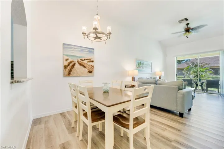 Open-concept living space featuring wood-finish flooring, a contemporary chandelier, and an arched pass-through window with a granite ledge