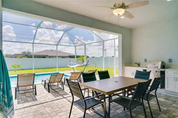 View of patio featuring a lanai, a fenced in pool, sink, ceiling fan, and grilling area