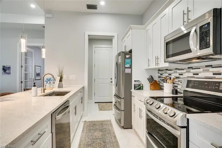 Kitchen featuring white cabinets, light tile patterned floors, stainless steel appliances, sink, and pendant lighting