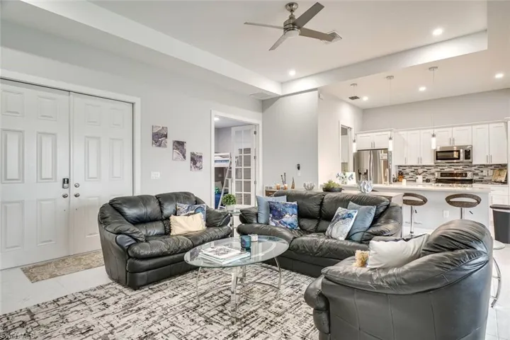 Living room featuring a raised ceiling, ceiling fan, and light tile patterned flooring