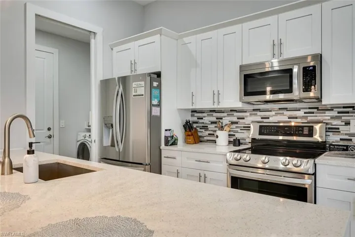 Kitchen with appliances with stainless steel finishes, backsplash, sink, and white cabinets