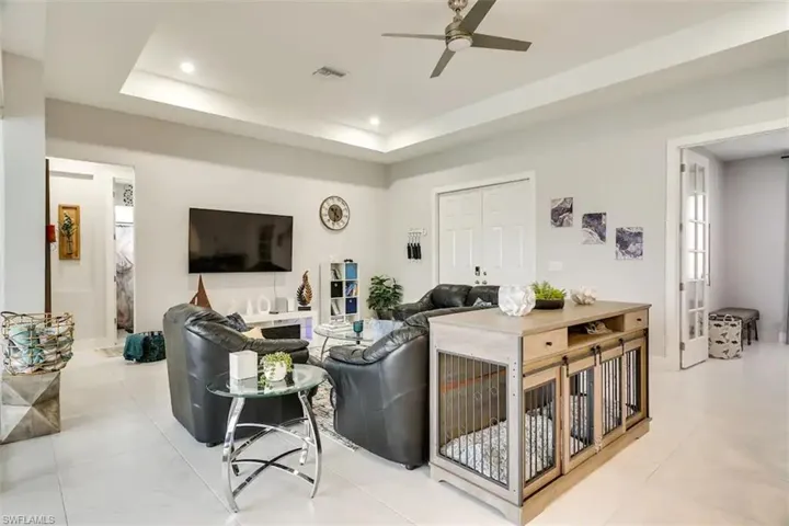 Living room featuring a tray ceiling, light tile patterned floors, and ceiling fan