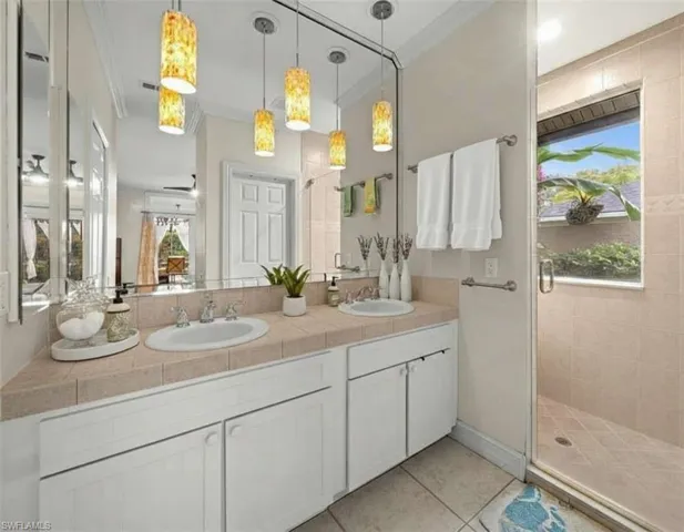 Bathroom with a shower stall, double vanity, light tile patterned floors, and crown molding
