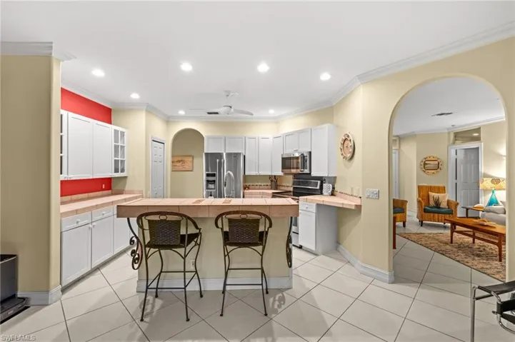 Kitchen with arched walkways, crown molding, tile counters, stainless steel appliances, and a kitchen breakfast bar