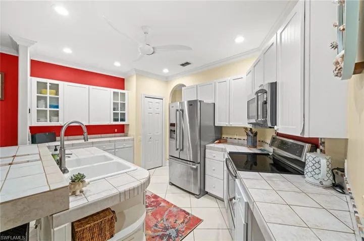 Kitchen featuring stainless steel appliances, glass insert cabinets, tile counters, crown molding, and white cabinets
