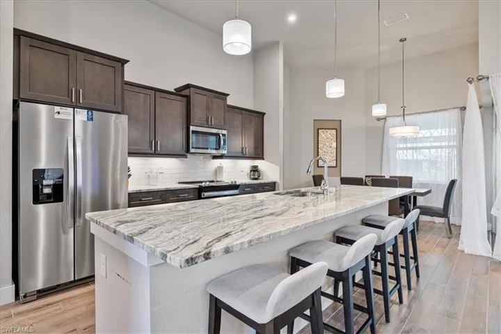 Kitchen with appliances with stainless steel finishes, dark brown cabinetry, a kitchen island with sink, tasteful backsplash, and light wood-type flooring
