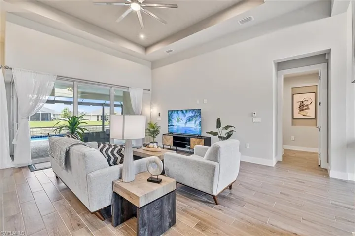 Living area with a ceiling fan, light wood finished floors, a tray ceiling, recessed lighting, and a high ceiling